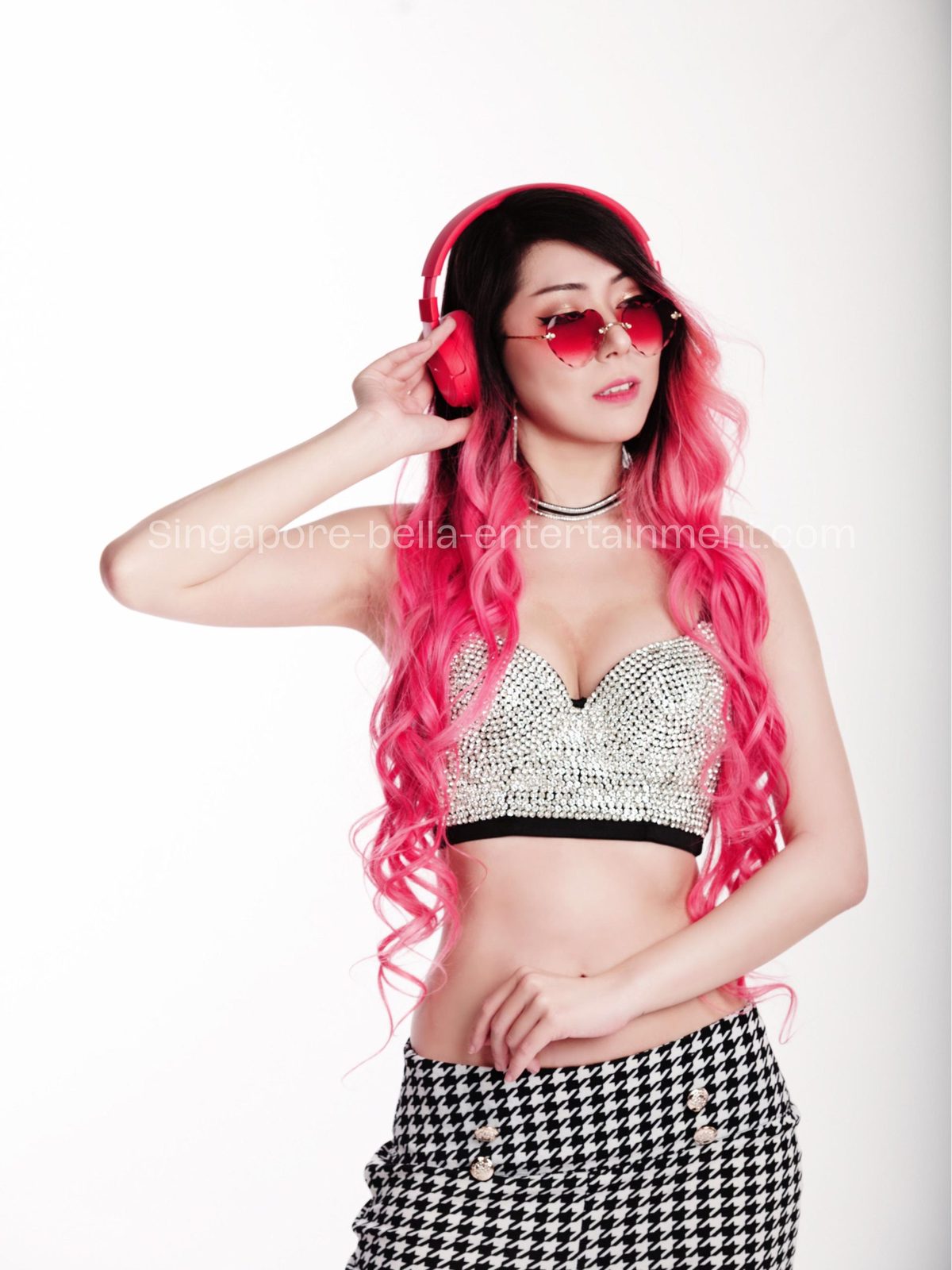 Woman with pink hair wearing a black and white dress and red headphones, posing for a picture against a white, Hire DJ Singapore