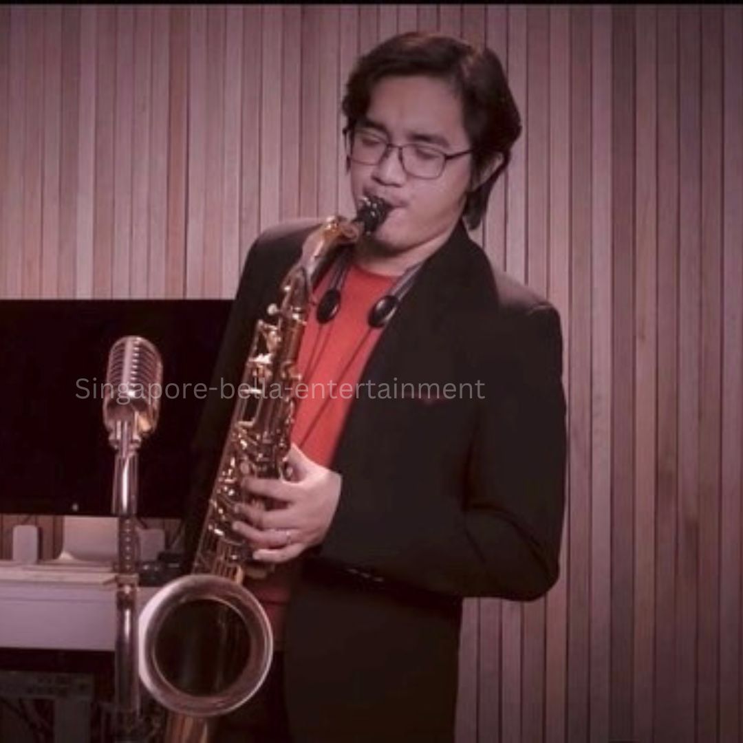 Man in a suit playing a saxophone in front of a microphone, with a monitor and other objects on a table in, Saxophonist
