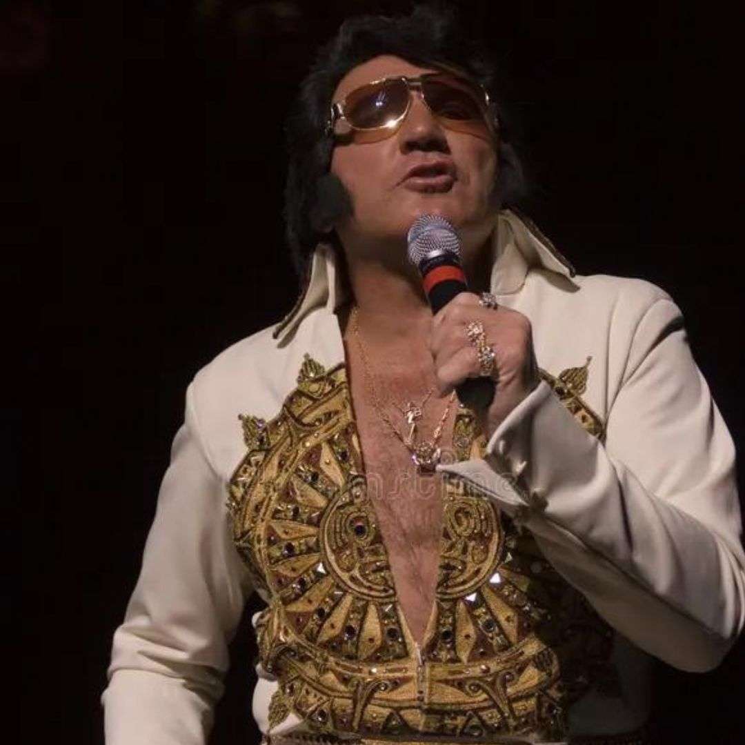 Man in a white suit and sunglasses holding a microphone, with a dark background, Impersonator for Hire