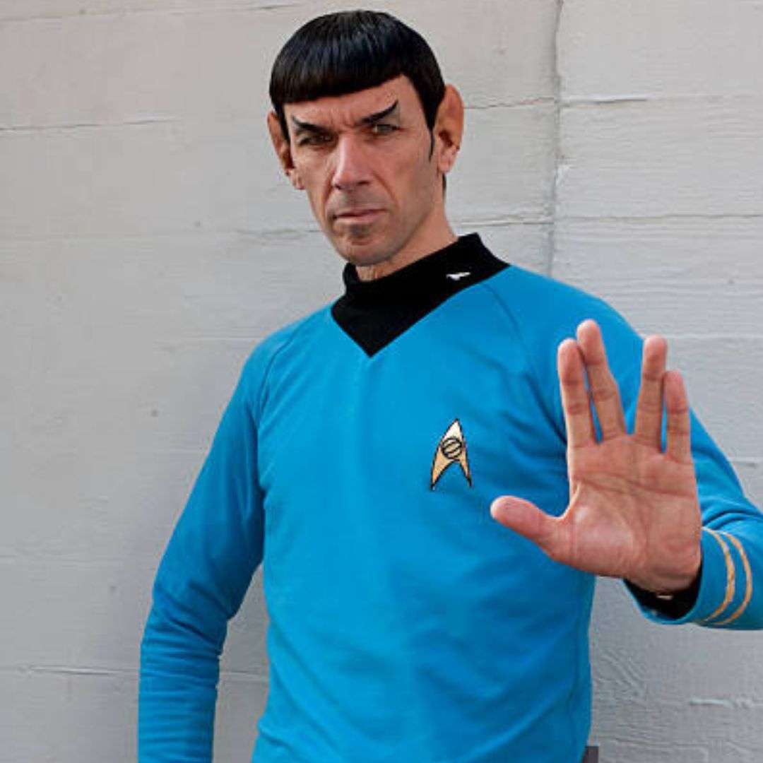 Man in a blue shirt standing in front of a wall, waving his hand, Impersonator for Hire