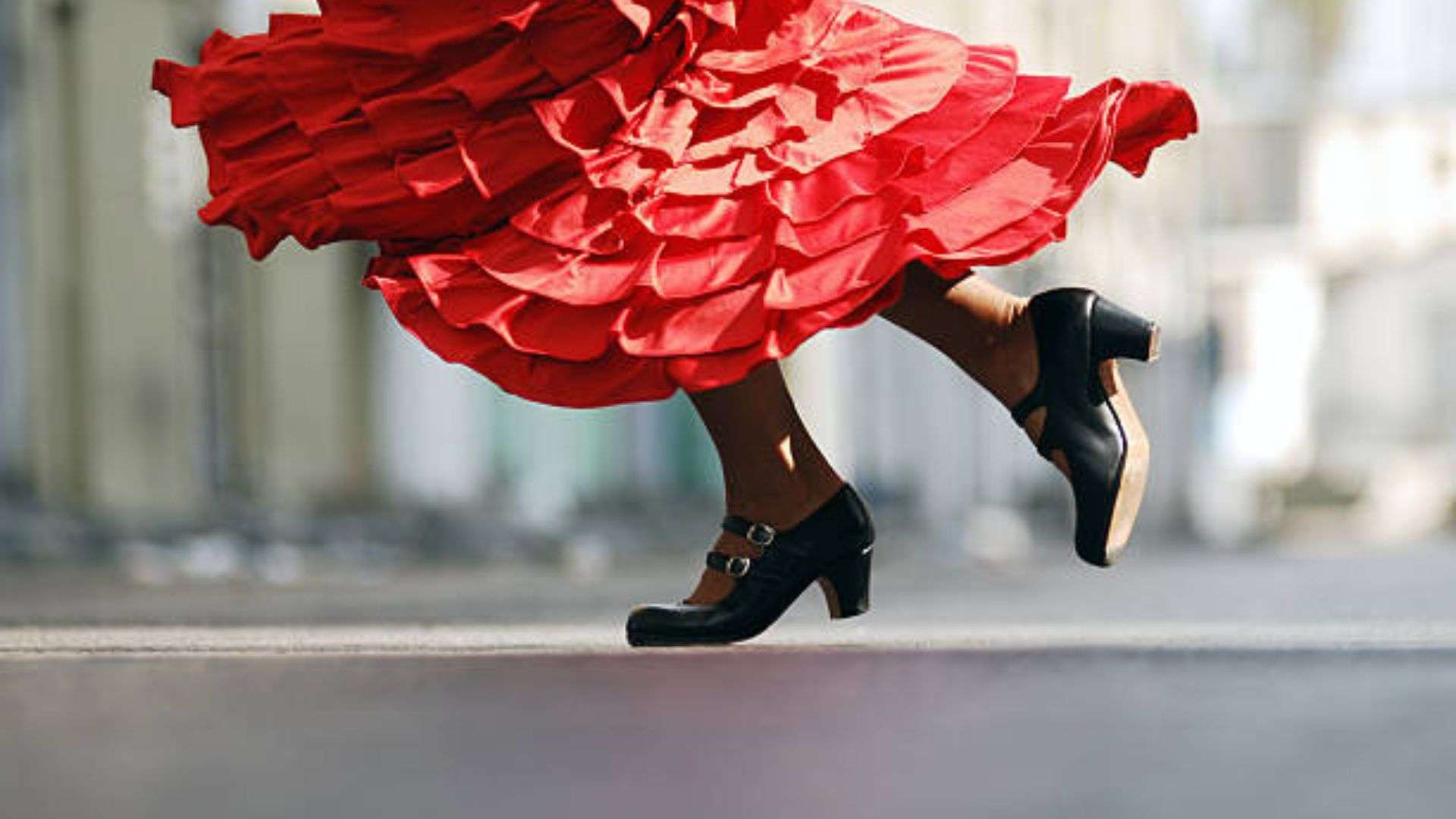 Woman in a red dress and black shoes dancing flamenco on the street, with a blurred background, Flamenco Dancer for Hire