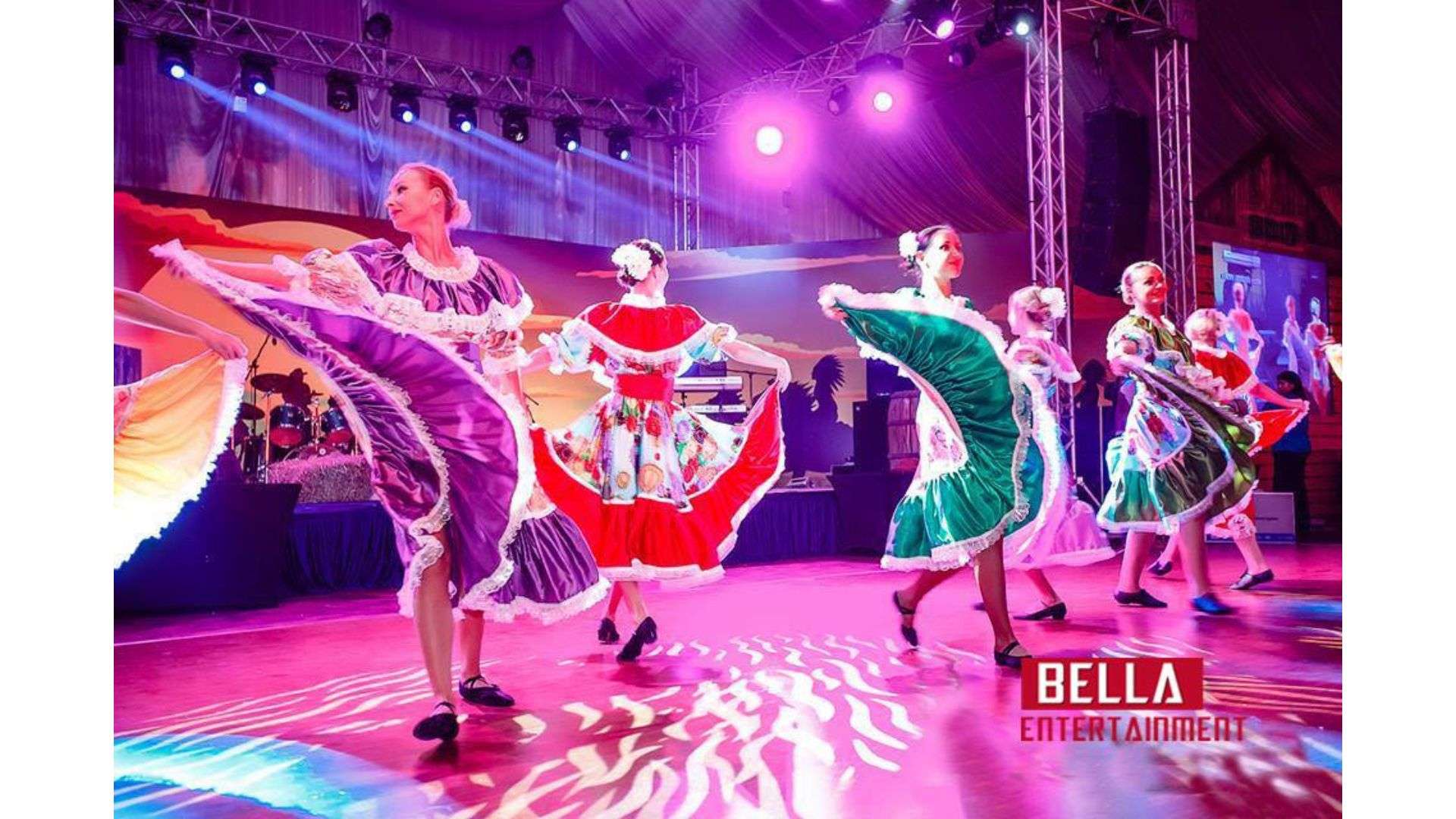 Group of women in colorful dresses dancing on a stage, illuminated by lights attached to the rods at the top, Flamenco Dancer for Hire