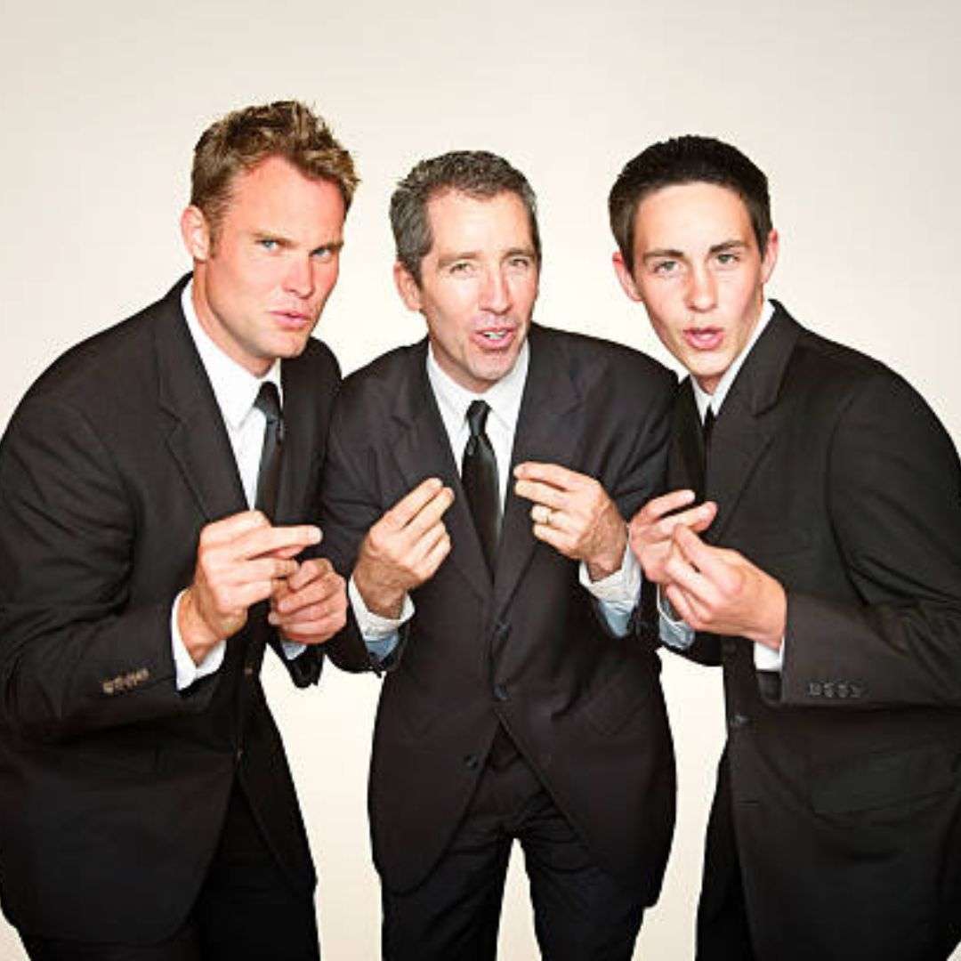 Three men in black blazers, white shirts, and black ties standing next to each other in front of a white, Musicians