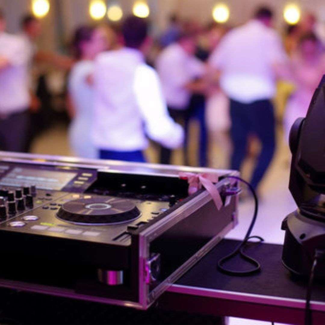 DJ mixer sitting on top of a table next to a crowd of people, illuminated by lights, Musicians