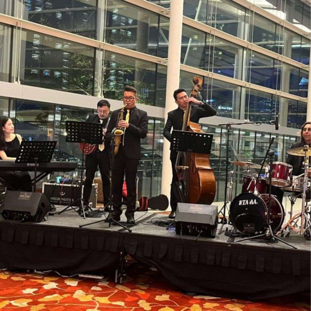Group of people playing musical instruments on a stage in front of a building with glass walls and pillars, Hire Gala Dinner Performance in Singapore