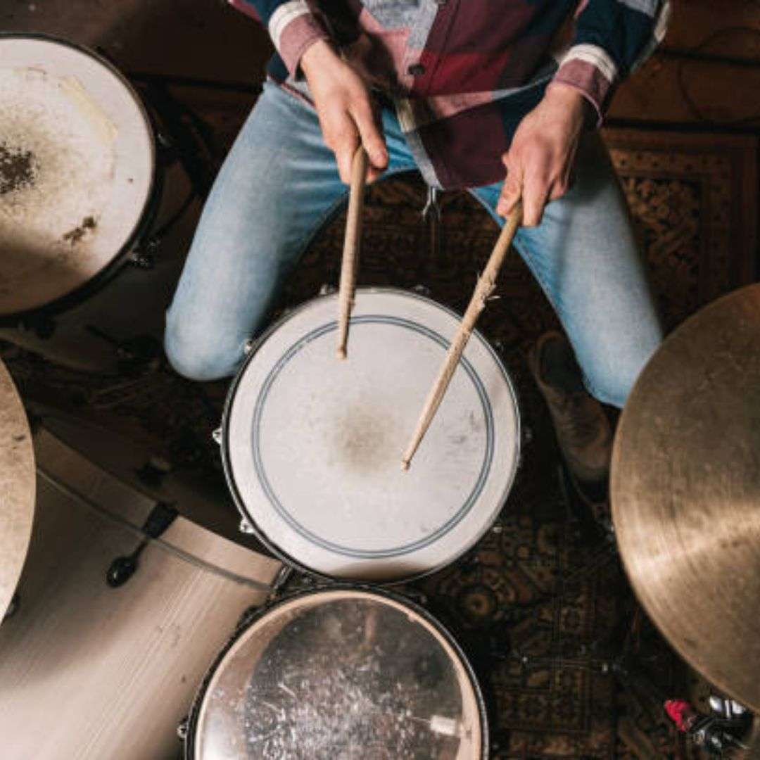 Man sitting on the floor playing drums with drumsticks in his hands, Hire Drummers in Singapore