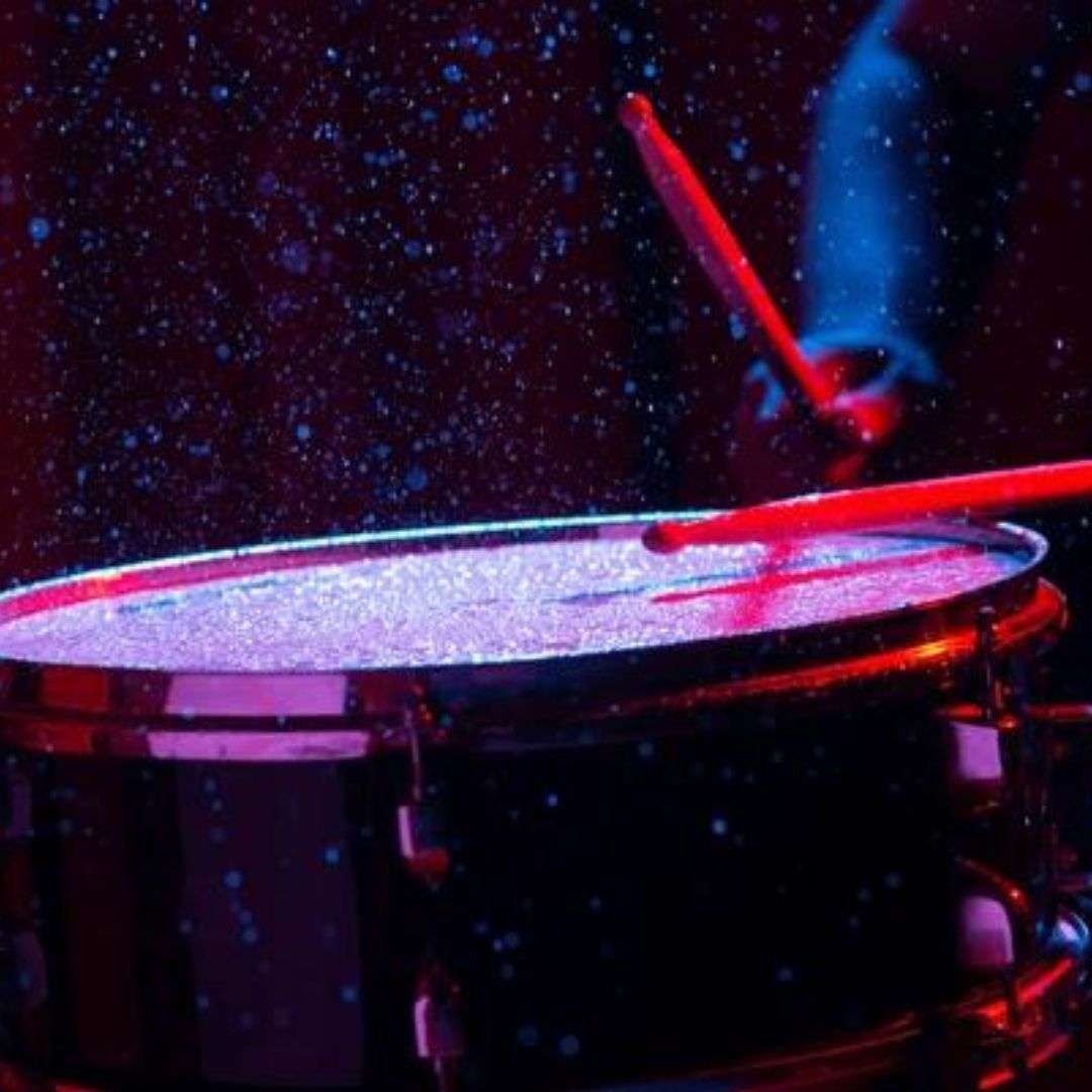 Person playing a drum set in a dark room, with two drumsticks in their hands, LED Water Drummer for Hire