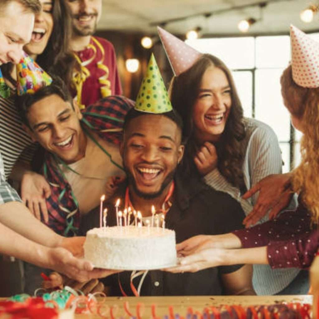 Group of people gathered around a table with a birthday cake adorned with lit candles