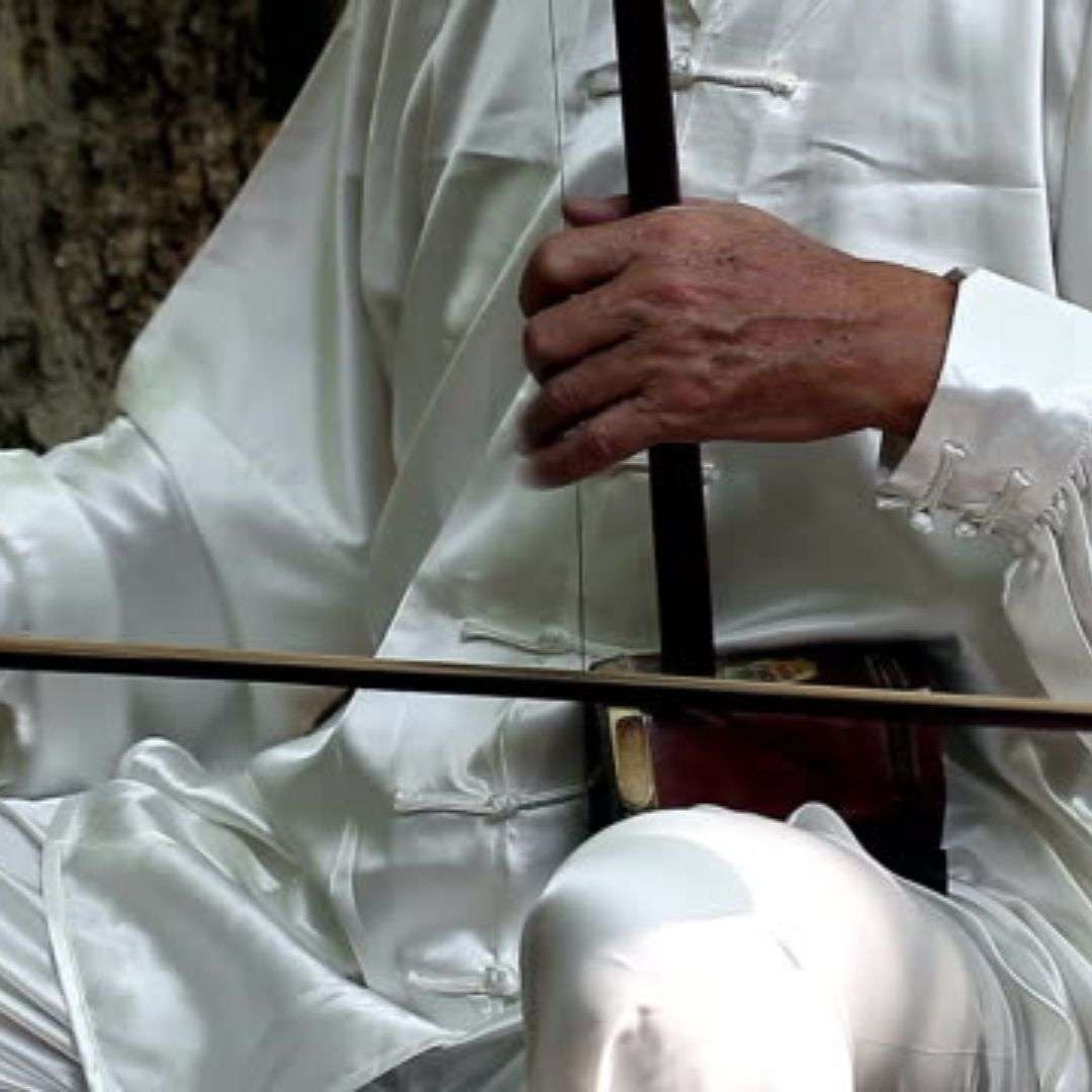 Man in a white robe sitting on a bench, holding a stick in his hand, Hire Er Hu Player in Singapore Man in a white robe sitting on a bench, holding a stick in his hand, Hire Er Hu Player in Singapore