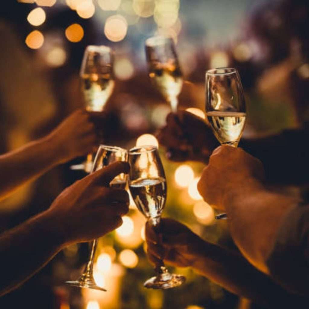 Group of people toasting with champagne glasses in their hands, illuminated by the lights in the background